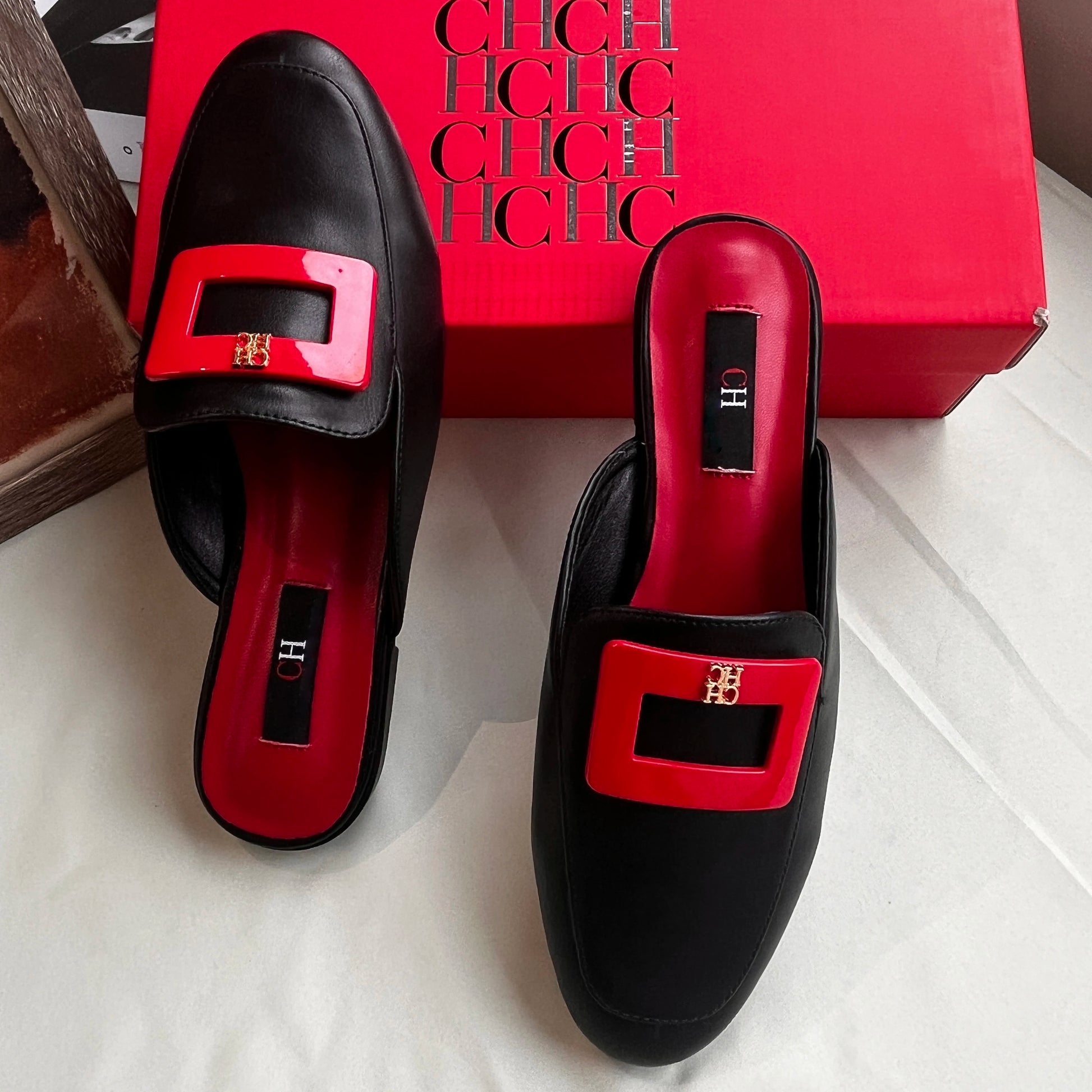 Black shoes with red buckles in front of a red box with 'H' branding.