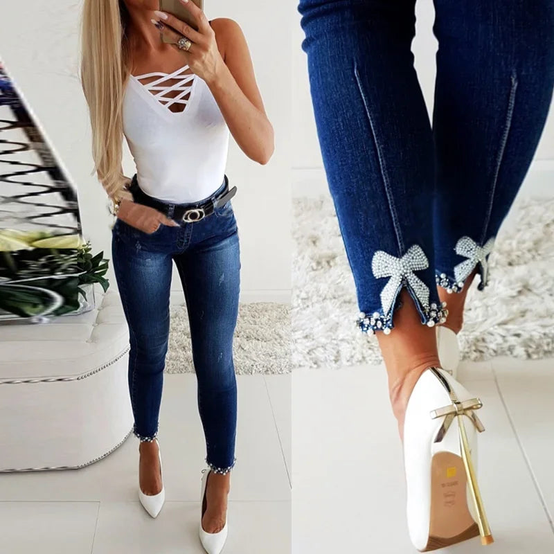 Woman wearing a white bodysuit and blue jeans on a white background. Women’s pencil cut jeans, high waist, vintage washed denim with pearl detail. Ankle length skinny denim trousers, stylish casual UK look.