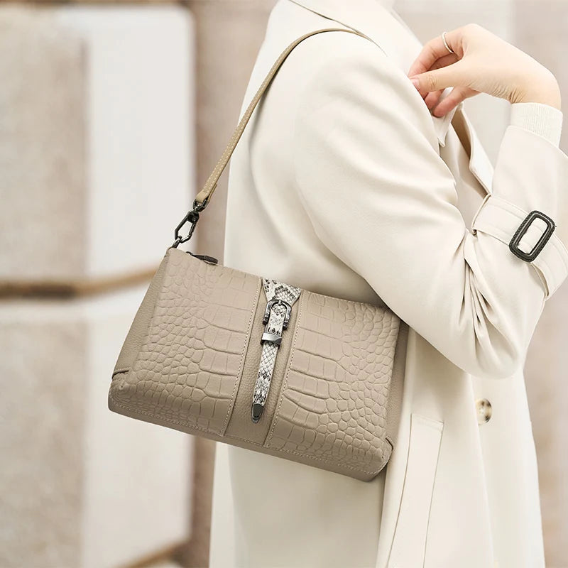 Beige handbag with crocodile texture held by a person wearing a beige coat. Genuine leather women’s shoulder messenger bag in black and gray. Soft cow leather, flap style with zipper closure. Perfect versatile bag for all seasons.