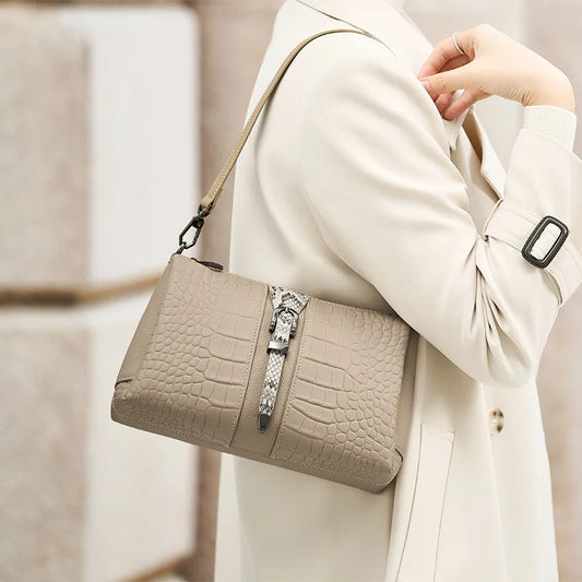Beige handbag with crocodile texture held by a person wearing a beige coat. Genuine leather women’s shoulder messenger bag in black and gray. Soft cow leather, flap style with zipper closure. Perfect versatile bag for all seasons.