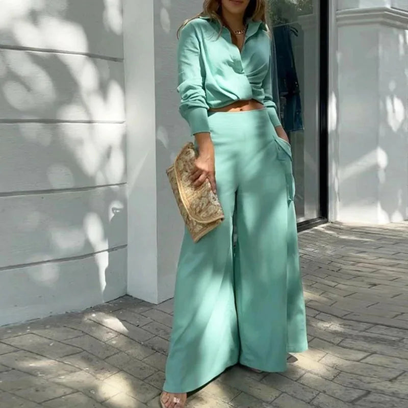 Person wearing a mint green outfit with wide-leg pants and holding a clutch. Women's elegant pants set with long sleeve crop shirt and high waist wide leg trousers. Office lady style. Solid, flattering, comfortable fit.