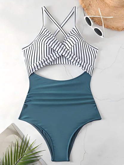 Blue and black striped swimsuit on a white surface with sunglasses and a plant.