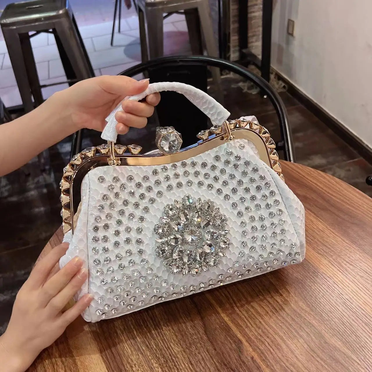 Decorative handbag with rhinestone embellishments on a wooden table. Large genuine leather dumpling bag with diamond rhinestone clip and lock clasp. Soft handle, multiple compartments. Fashionable shoulder tote for women.