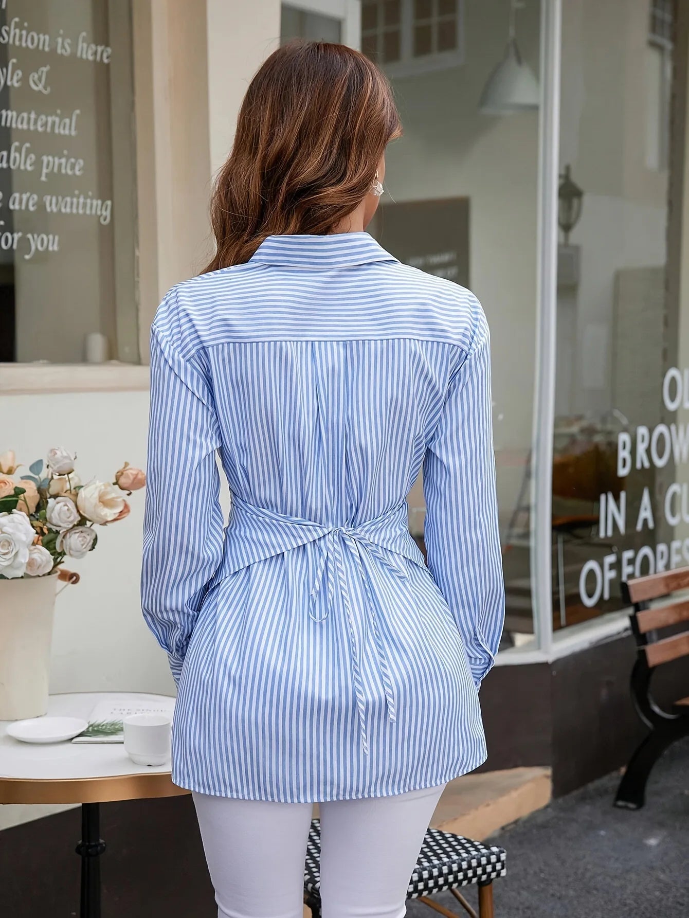 Woman wearing a blue and white striped shirt in front of a store window.