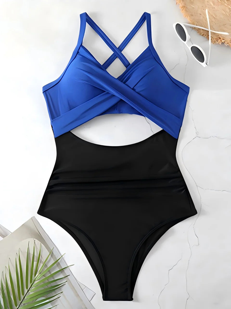 Black and blue swimsuit on a white surface with sunglasses and a plant.