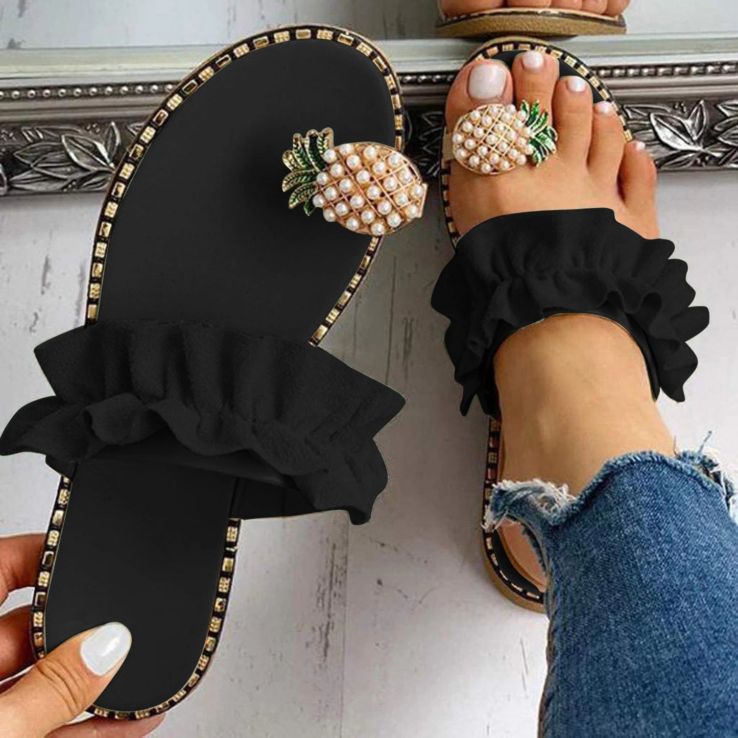 Black sandals with pineapple embellishments worn by a person with blue jeans.