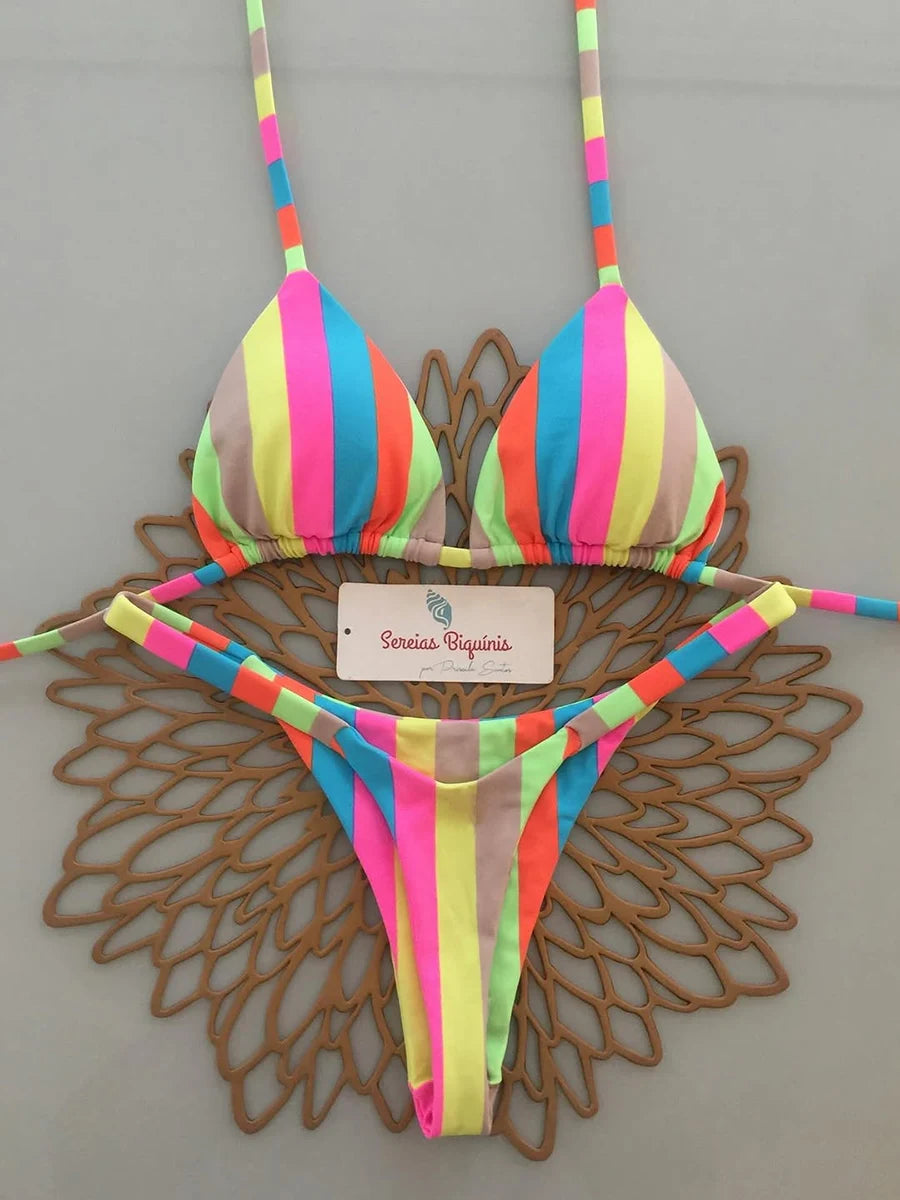 Colorful striped bikini set on a decorative wooden stand against a gray background