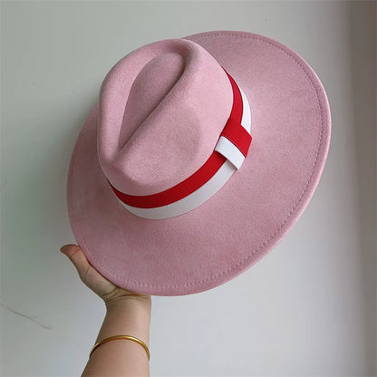 Pink fedora hat with a red and white band held by a hand on a light gray background