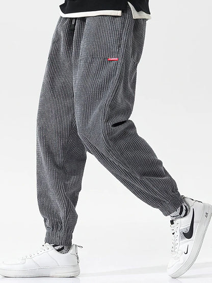 Gray corduroy pants worn with white sneakers on a light gray background. Men's baggy corduroy jogger pants, tech fleece sweatpants, autumn winter harem trousers, elastic waist, thermal, UK FTF Market.