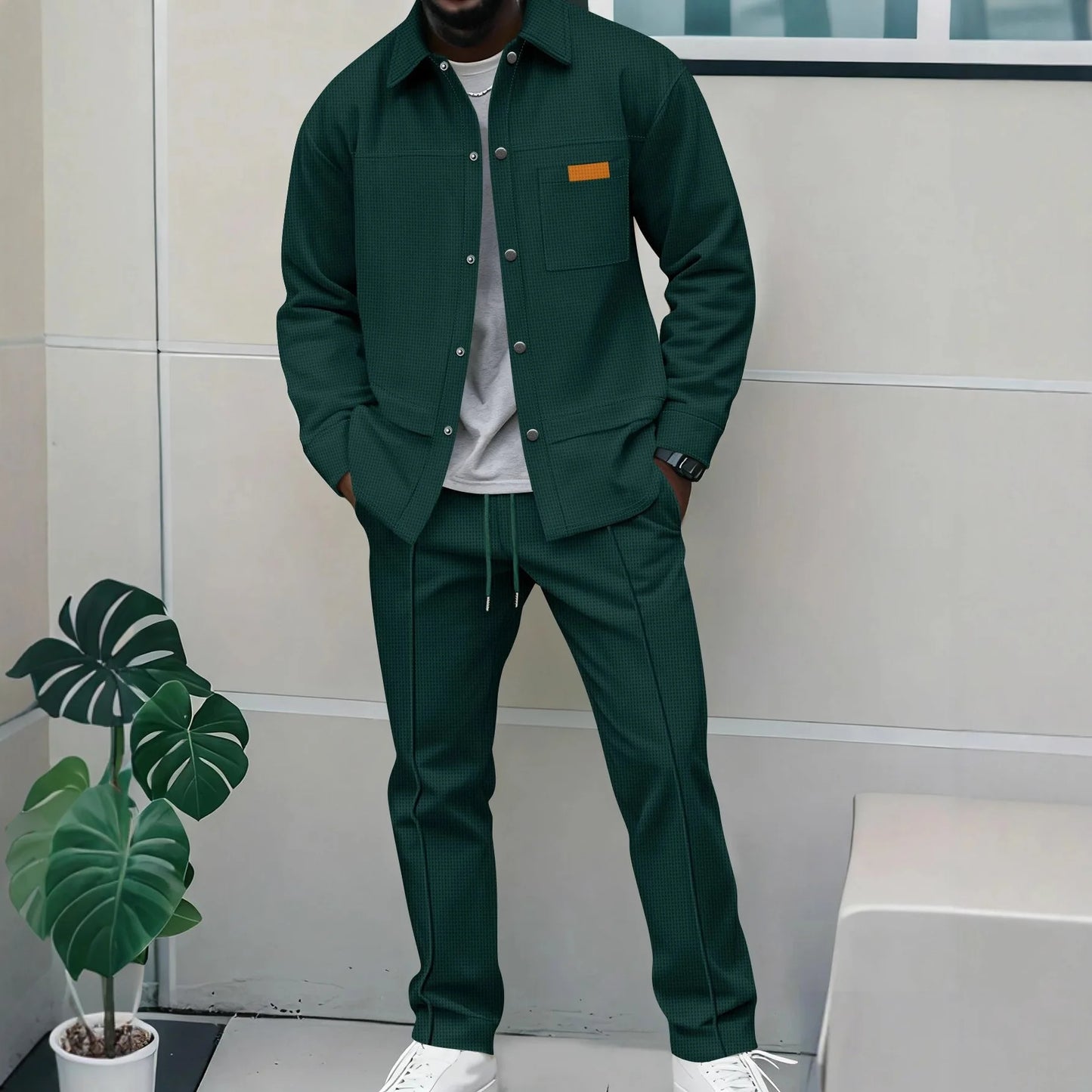 Person wearing a green outfit standing indoors with a plant in the foreground.