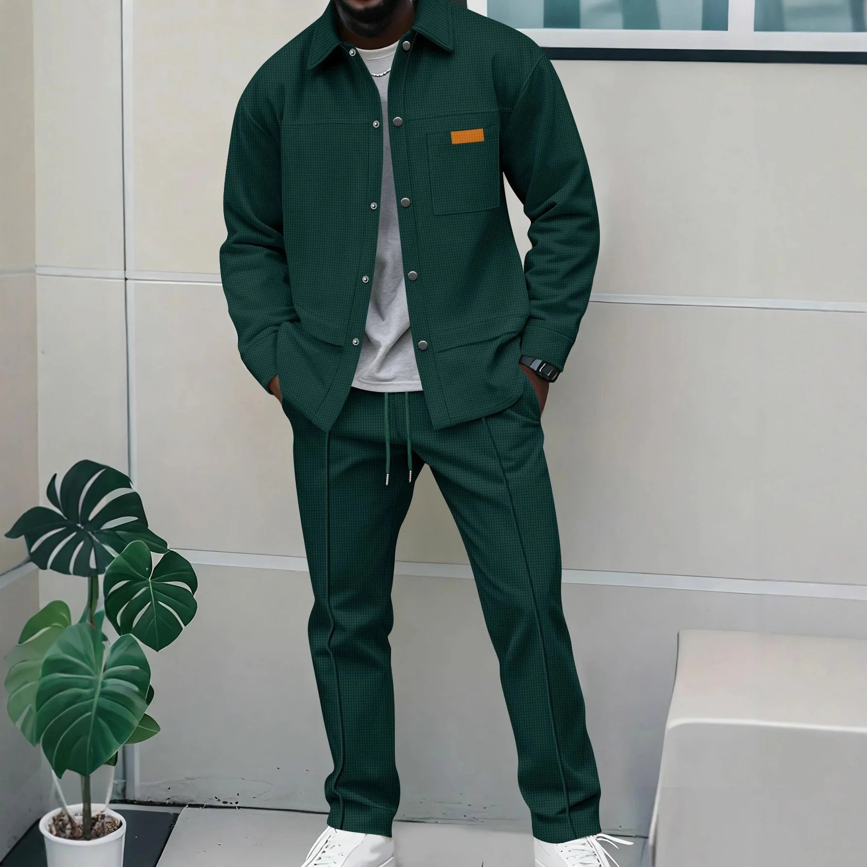 Person wearing a green outfit standing indoors with a plant in the foreground.