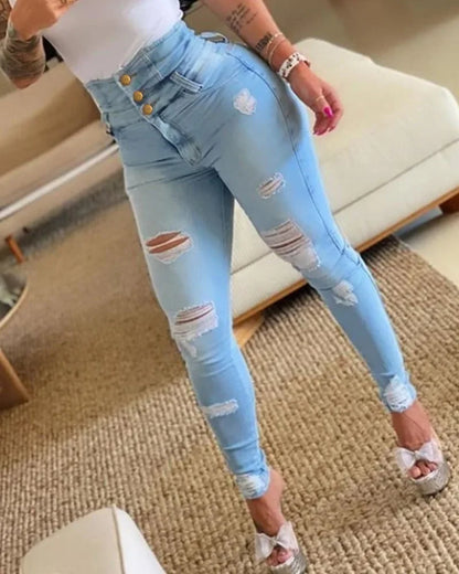 Person wearing light blue ripped jeans indoors on a carpeted floor. Women’s slim pencil jeans, high waist bodycon fit. Casual sheath denim trousers with button detail, ankle length. Trendy Y2K style UK.