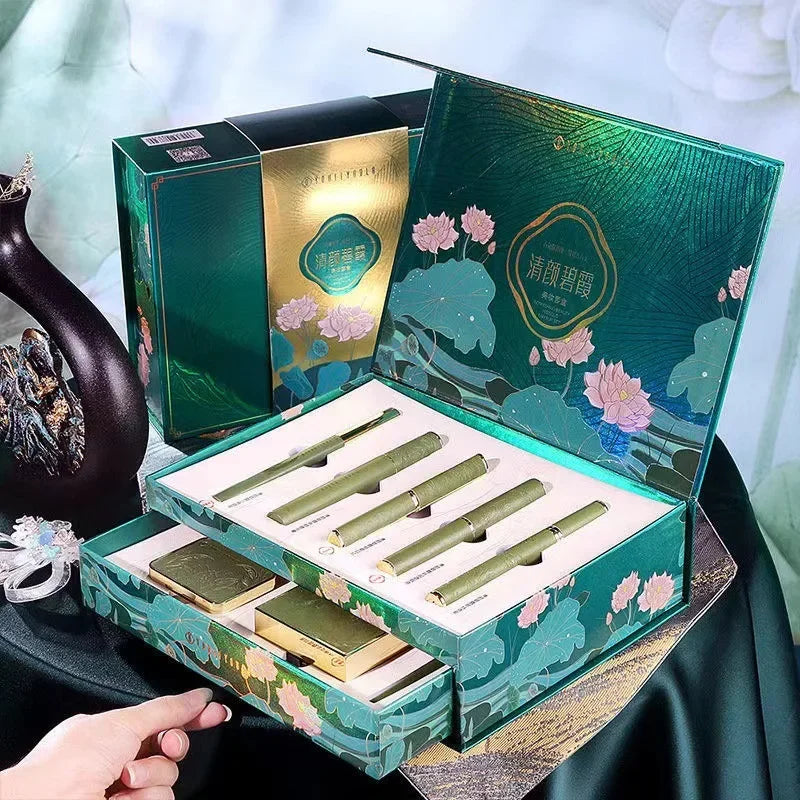 Green decorative box with floral designs containing green items on a white background. Christmas makeup gift box with BB cream, lipstick, eyeshadow, eyebrow pencil, and brushes. Holiday beauty set for women & girls.