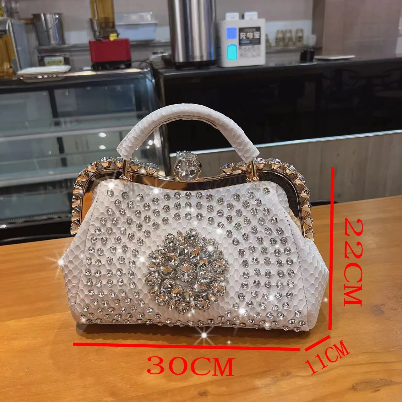 Decorative handbag with rhinestone embellishments on a wooden surface, with measurements indicated.. Large genuine leather dumpling bag with diamond rhinestone clip and lock clasp. Soft handle, multiple compartments. Fashionable shoulder tote for women.