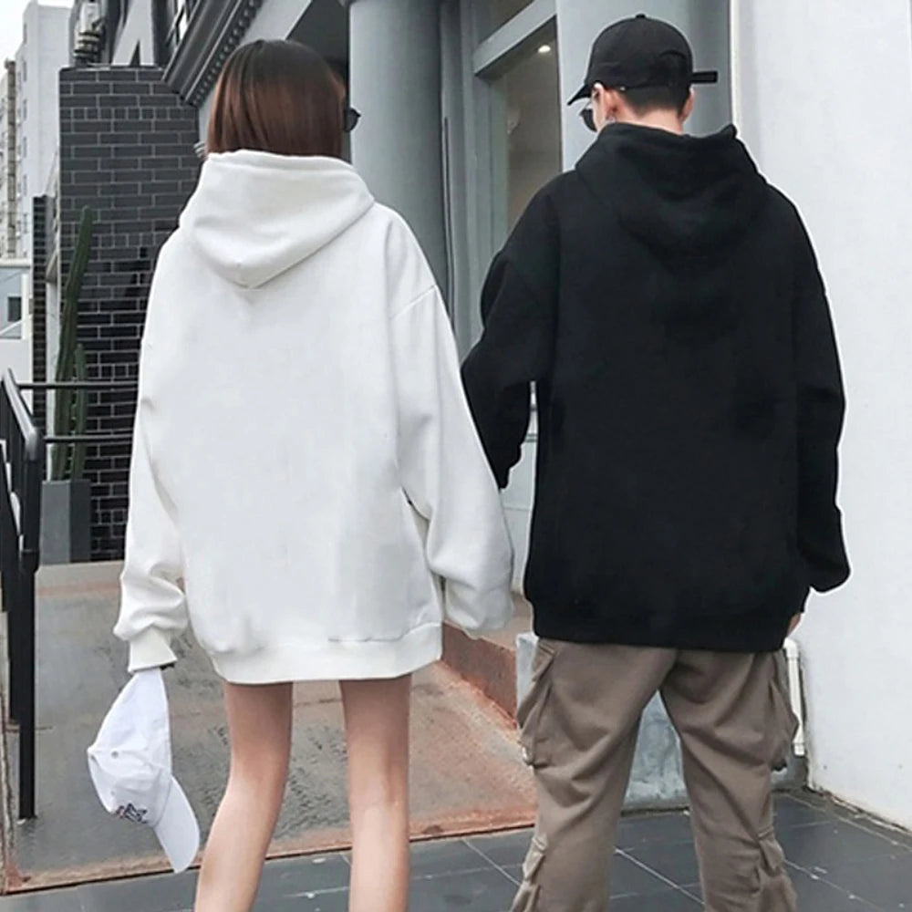 Two people wearing hoodies walking together on a street.