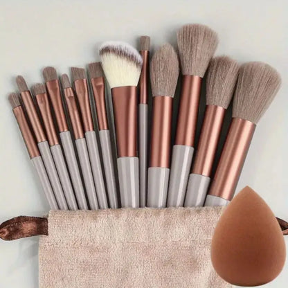Set of makeup brushes with rose gold and gray handles, a beige pouch, and a brown sponge on a light background. Soft fluffy makeup brush set with wool fiber bristles and plastic handles. Complete set for powder, foundation, eyeshadow, and beauty blending.
