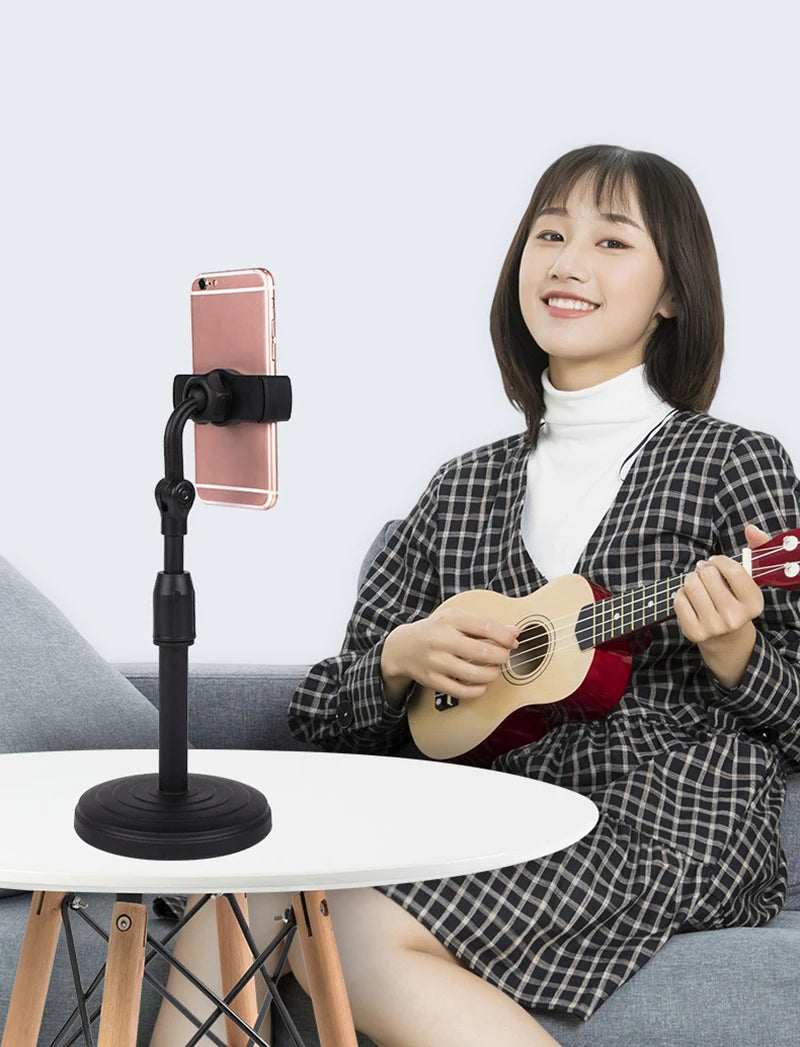 Woman playing a ukulele with a smartphone on a stand in front of her. Aluminum alloy desktop tripod phone holder stand bracket for iPhone & smartphones. Portable stable tripod perfect for photography, video, live calls.