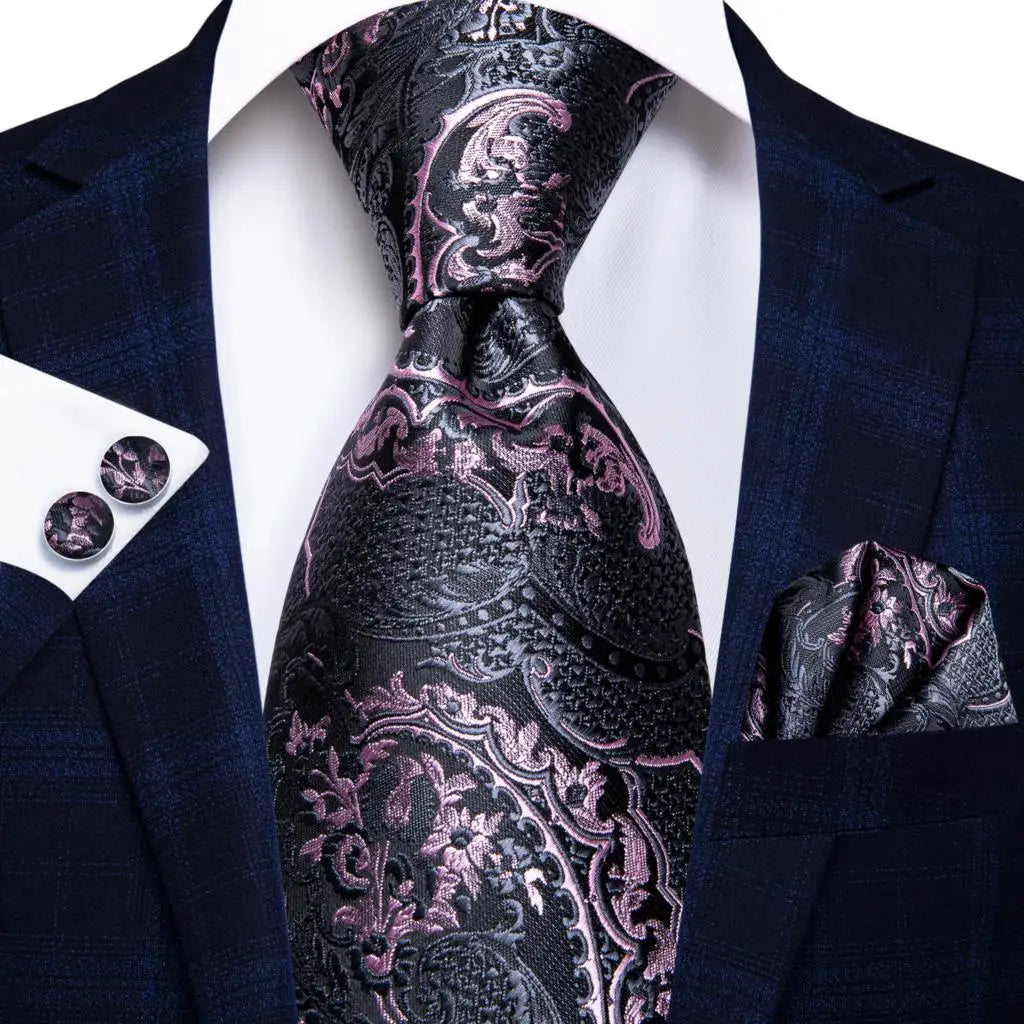Navy suit with a patterned pink and black tie, pocket square, and cufflinks on a white background. Men’s luxury paisley silk tie and pocket square set, 8.5cm wide, for business or wedding. Red formal necktie, ftf fashion UK.