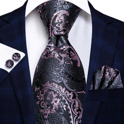Navy suit with a patterned pink and black tie, pocket square, and cufflinks on a white background. Men’s luxury paisley silk tie and pocket square set, 8.5cm wide, for business or wedding. Red formal necktie, ftf fashion UK.