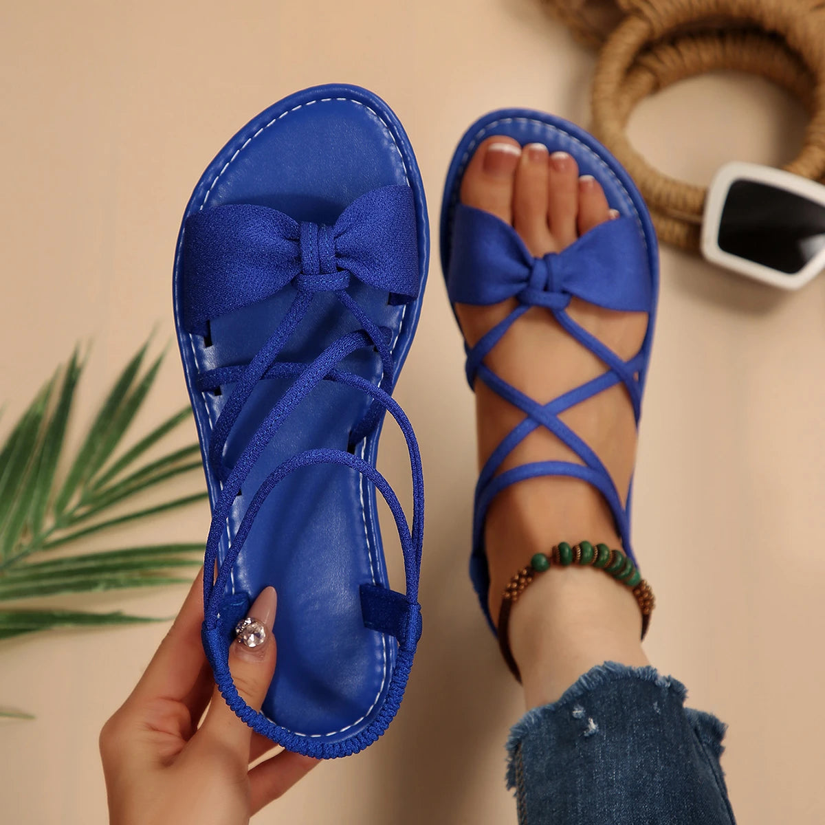 Blue sandals with bow detail held by a hand on a beige background