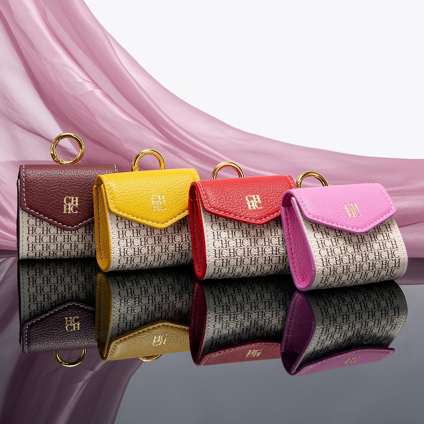 Four small leather pouches in different colors with a brand logo on a reflective surface.