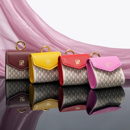 Four small leather pouches in different colors with a brand logo on a reflective surface.