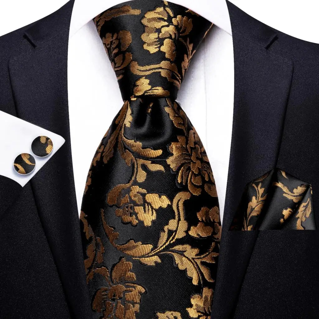 Black suit with gold floral tie, pocket square, and cufflinks on a white background. Men’s luxury paisley silk tie and pocket square set, 8.5cm wide, for business or wedding. Red formal necktie, ftf fashion UK.
