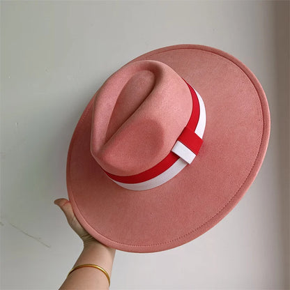 Pink hat with a red and white band held by a hand against a light gray background