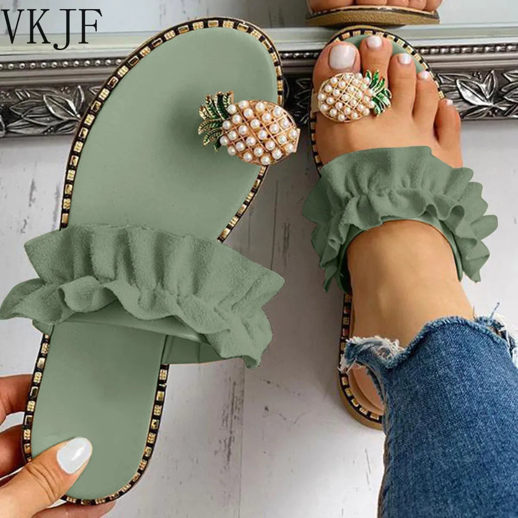 Green sandals with ruffles and pearl embellishments worn by a person in jeans.