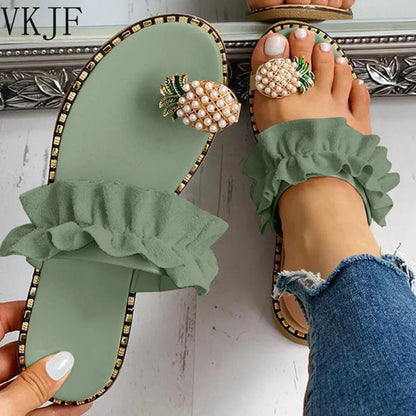 Green sandals with ruffles and pearl embellishments worn by a person in jeans.