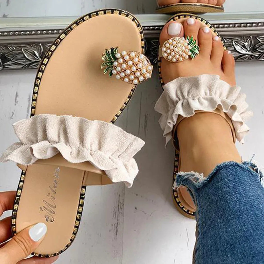 Beige sandals with ruffles and decorative pineapple embellishments worn by a person.