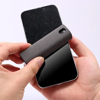 Person holding a smartphone with a black case on a white background. 4in1 microfiber screen cleaner spray with cloth for phones, tablets, computers, glasses. Portable, streak-free, safe for all screens, UK FTF Market.