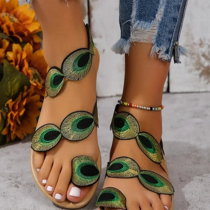 Sandals with peacock feather design worn by a person, with flowers in the background.