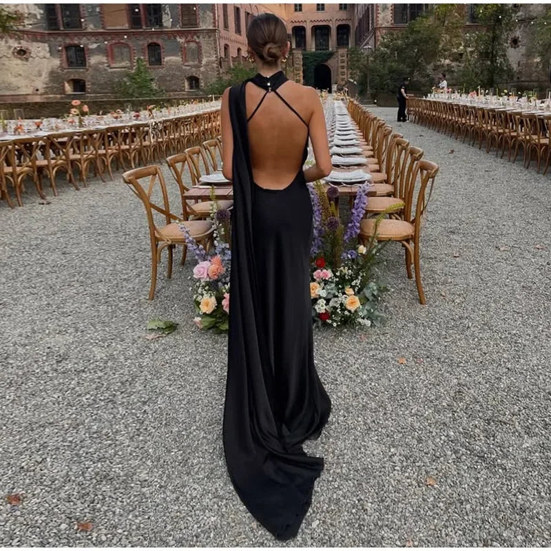 Person in a black evening gown standing in front of an outdoor dining setup with floral arrangements.