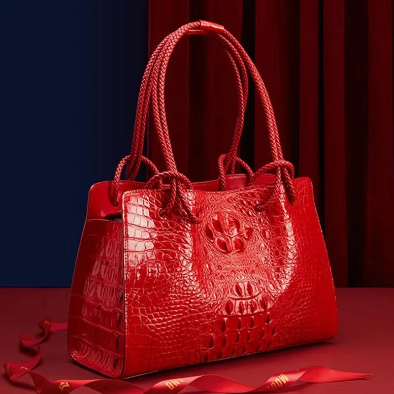 Red textured handbag with a decorative emblem on a red background. Luxury women’s tote bag in genuine red crocodile leather. Large capacity, stylish handle, fashion travel handbag. Perfect for shoulder or portable use UK.