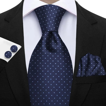 Navy blue tie with white polka dots paired with a matching pocket square and cufflinks on a suit. Elegant men’s 3-piece tie set: striped necktie, floral pocket square, matching cufflinks. Fashionable polyester accessories for formal occasions.