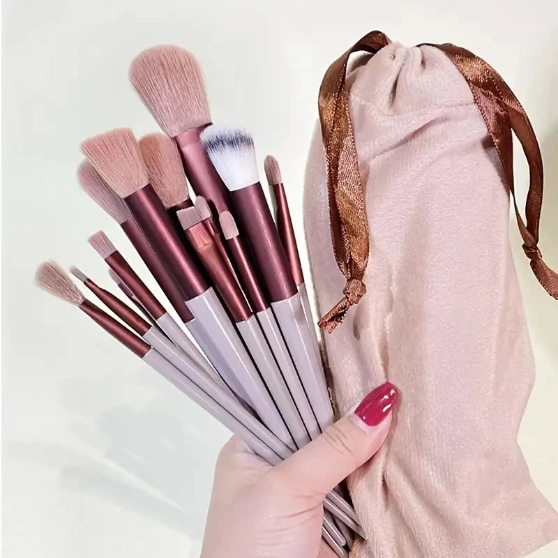 Set of makeup brushes with a pink drawstring bag on a light background. Soft fluffy makeup brush set with wool fiber bristles and plastic handles. Complete set for powder, foundation, eyeshadow, and beauty blending.