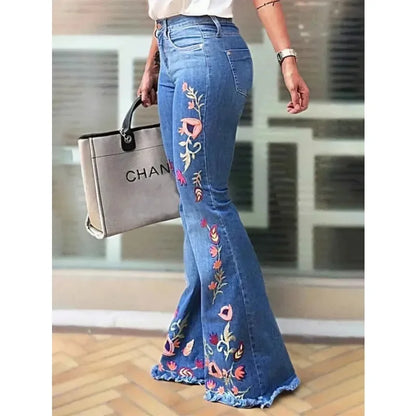 Woman wearing embroidered bell bottom jeans in blue denim, styled with a white top and handbag