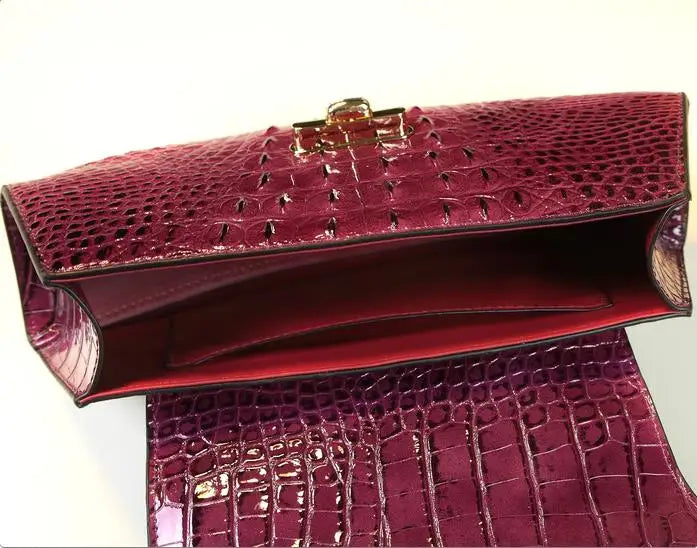 Red crocodile-patterned clutch bag with gold clasp on a light gray background