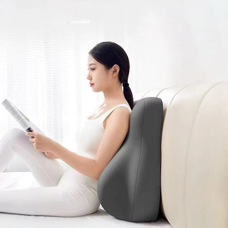 Woman using a back massager while reading a book on a white couch.