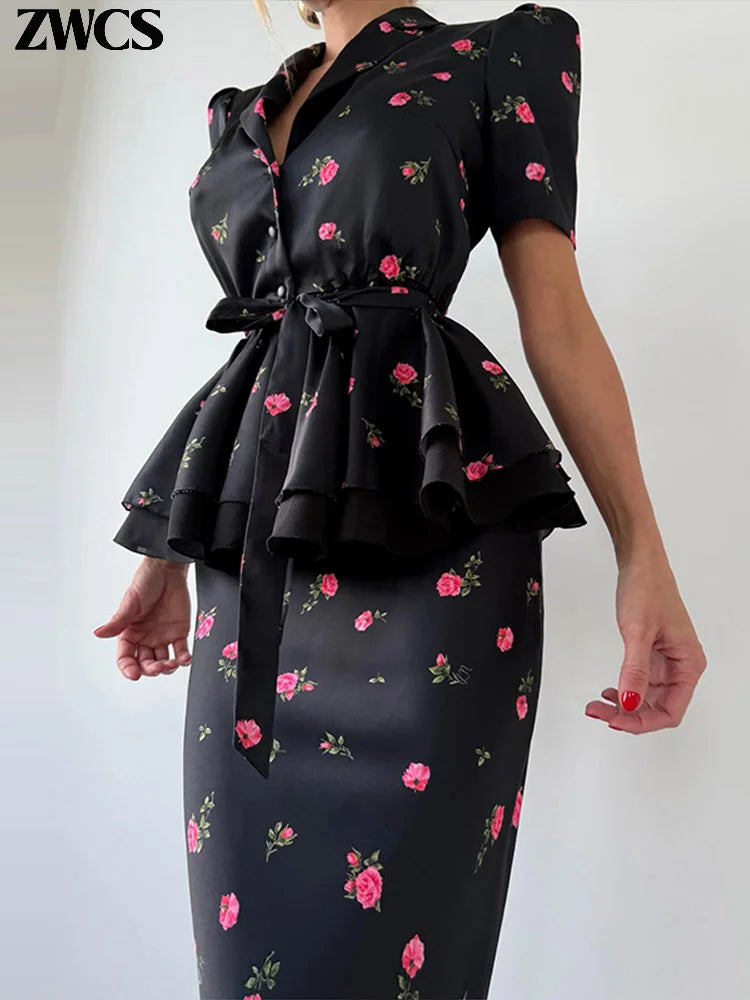 A woman wearing a black satin-like peplum dress with pink rose floral print, featuring short puff sleeves, a wrap-style neckline, and a self-tie waist belt. The brand name 'ZWCS' is visible in the top left corner.