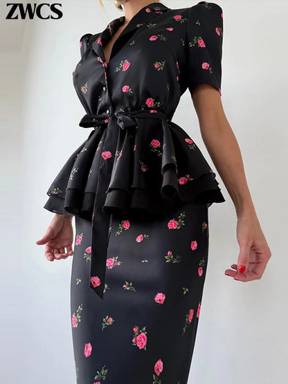 A woman wearing a black satin-like peplum dress with pink rose floral print, featuring short puff sleeves, a wrap-style neckline, and a self-tie waist belt. The brand name 'ZWCS' is visible in the top left corner.