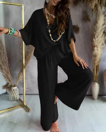 Woman wearing a black outfit with a gold necklace in a room with decorative plants.
