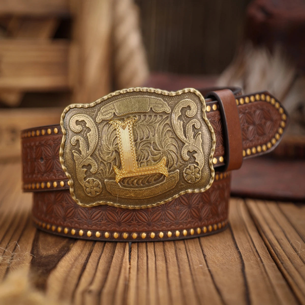Brown leather belt with a large gold buckle on a wooden surface