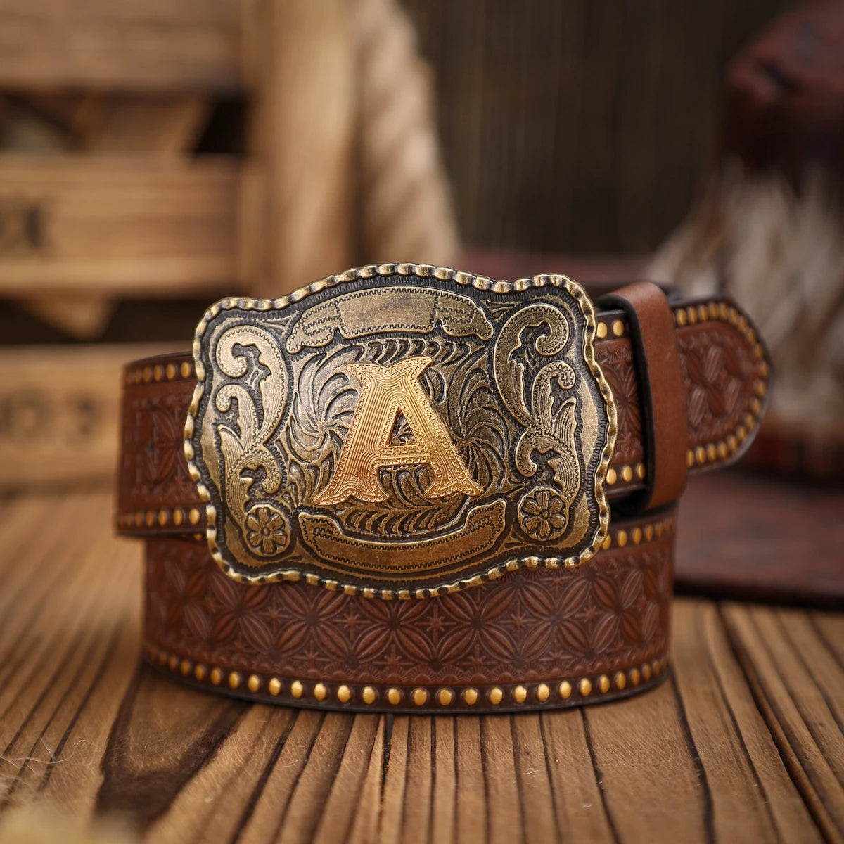 Brown leather belt with gold buckle featuring the letter 'A' on a wooden surface.