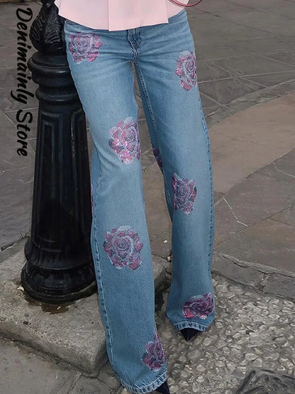 Flared jeans with floral patterns worn by a person on a sidewalk. Women’s denim jeans with flower rhinestones, loose wide leg, low waist, light wash. Stylish rhinestone casual trousers for UK fashion lovers.