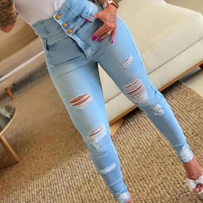 Light blue distressed jeans worn by a person indoors. Women’s slim pencil jeans, high waist bodycon fit. Casual sheath denim trousers with button detail, ankle length. Trendy Y2K style UK.