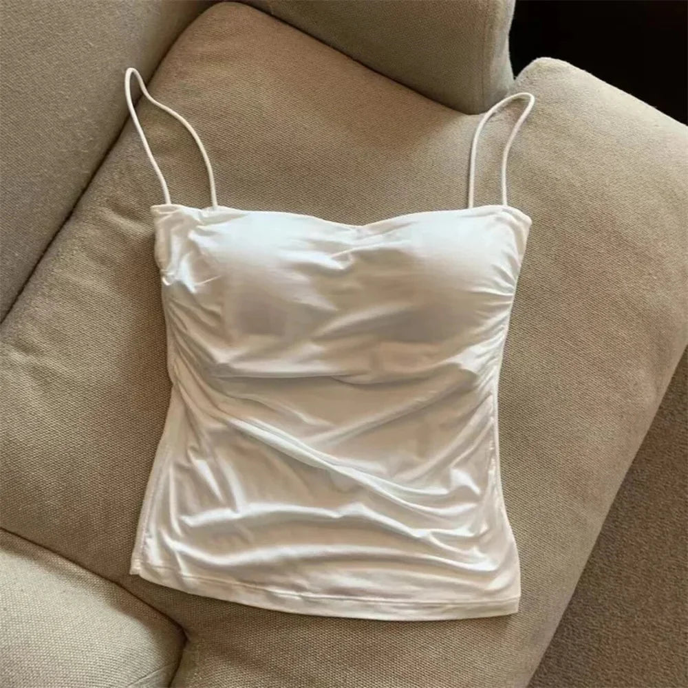 White satin camisole on a beige sofa. Corset taille cintrée élégant, sans manches avec pliage, coussinet poitrine, bretelles fines, top court solide, mode UK FTF Market.
