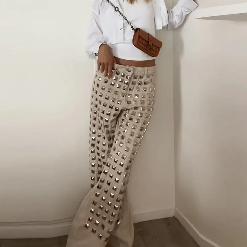Person wearing beige pants with studs, white shirt, and brown bag against a plain background. Women’s denim jeans with flower rhinestones, loose wide leg, low waist, light wash. Stylish rhinestone casual trousers for UK fashion lovers.