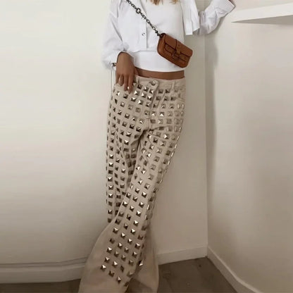 Person wearing beige pants with studs, white shirt, and brown bag against a plain background. Women’s denim jeans with flower rhinestones, loose wide leg, low waist, light wash. Stylish rhinestone casual trousers for UK fashion lovers.
